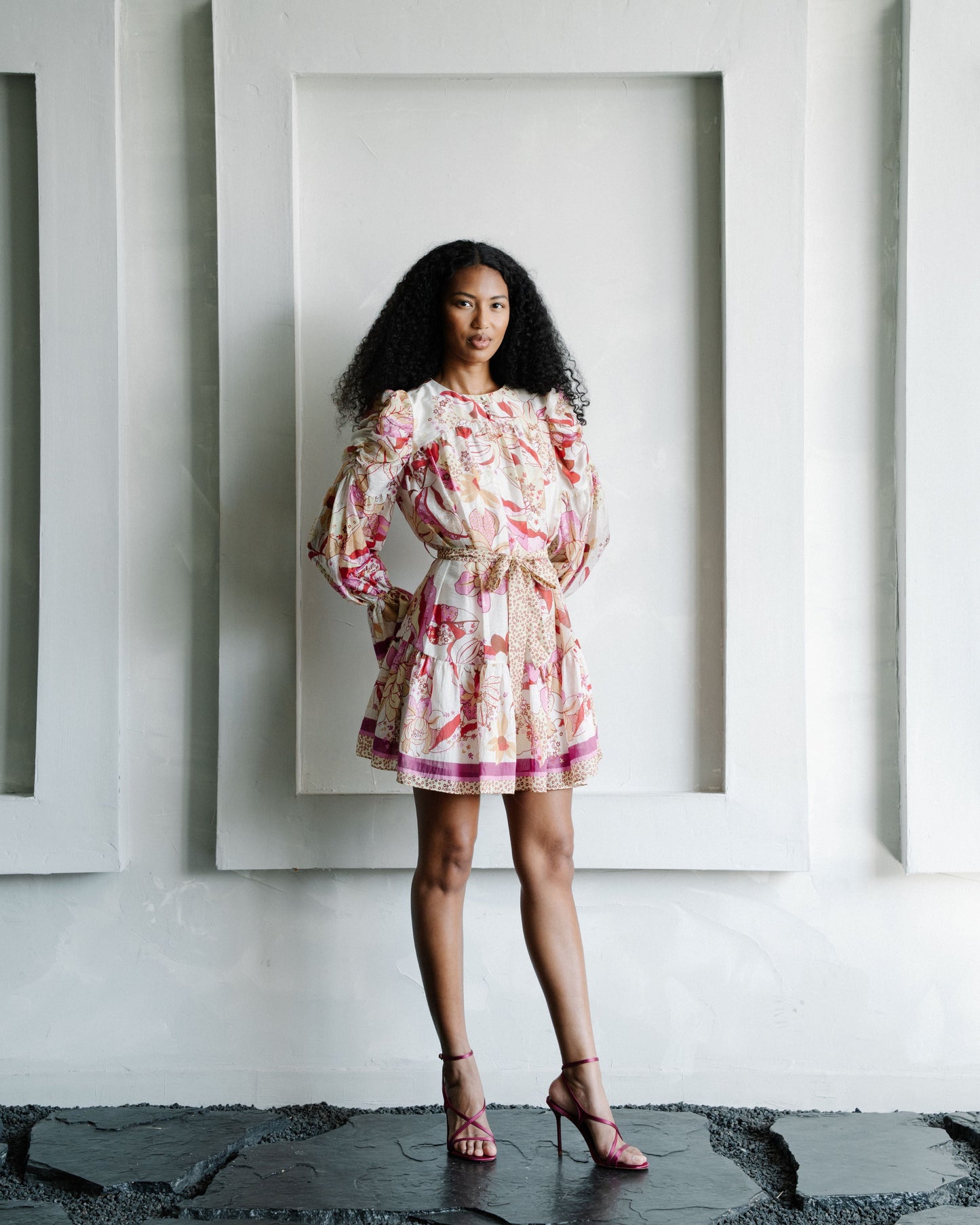 Woman in a floral dress standing in front of white wall with framed pictures