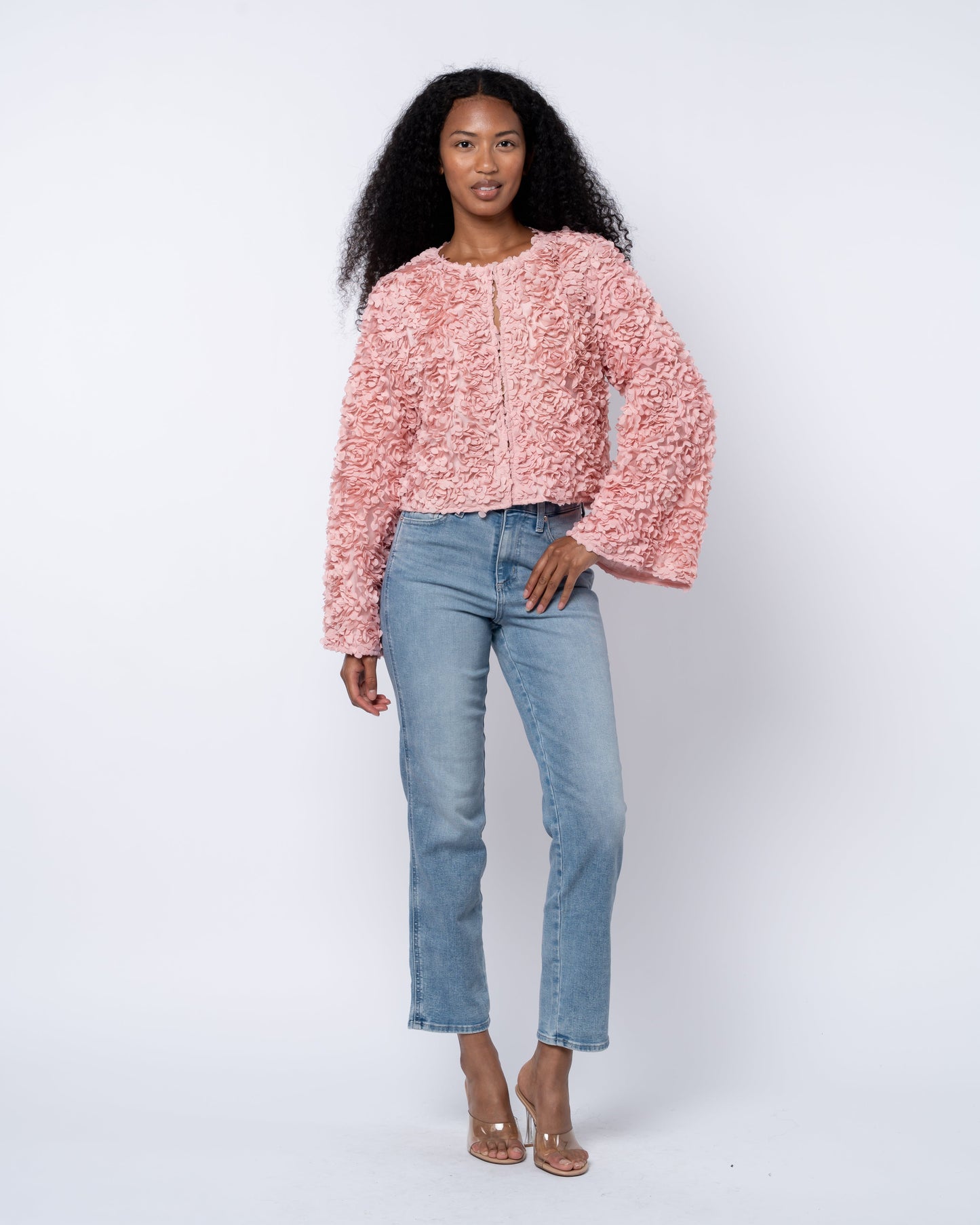 Woman wearing a pink textured sweater and blue jeans on a white background
