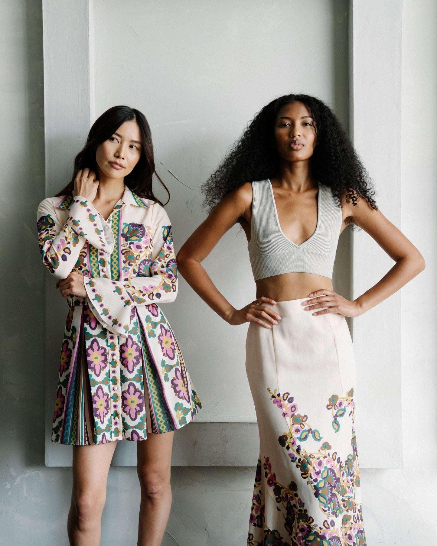 Two women posing in stylish outfits against a neutral background