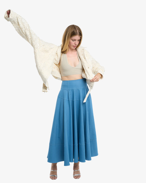 Load image 1 in gallery view. Woman wearing a white jacket, beige top, and blue skirt on a white background