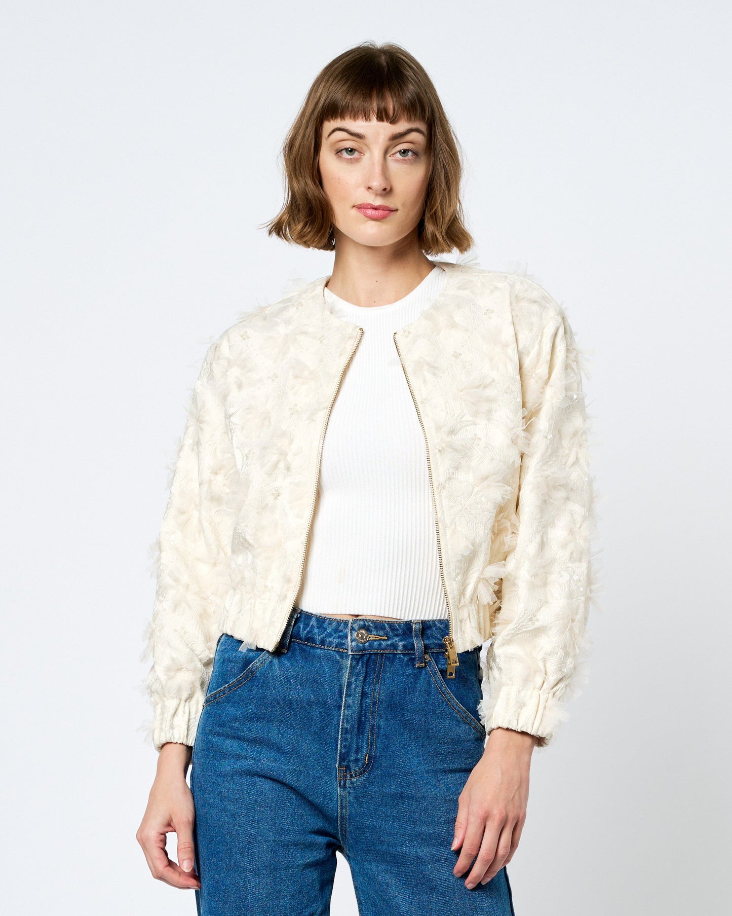 Woman wearing a cream jacket and blue jeans on a white background