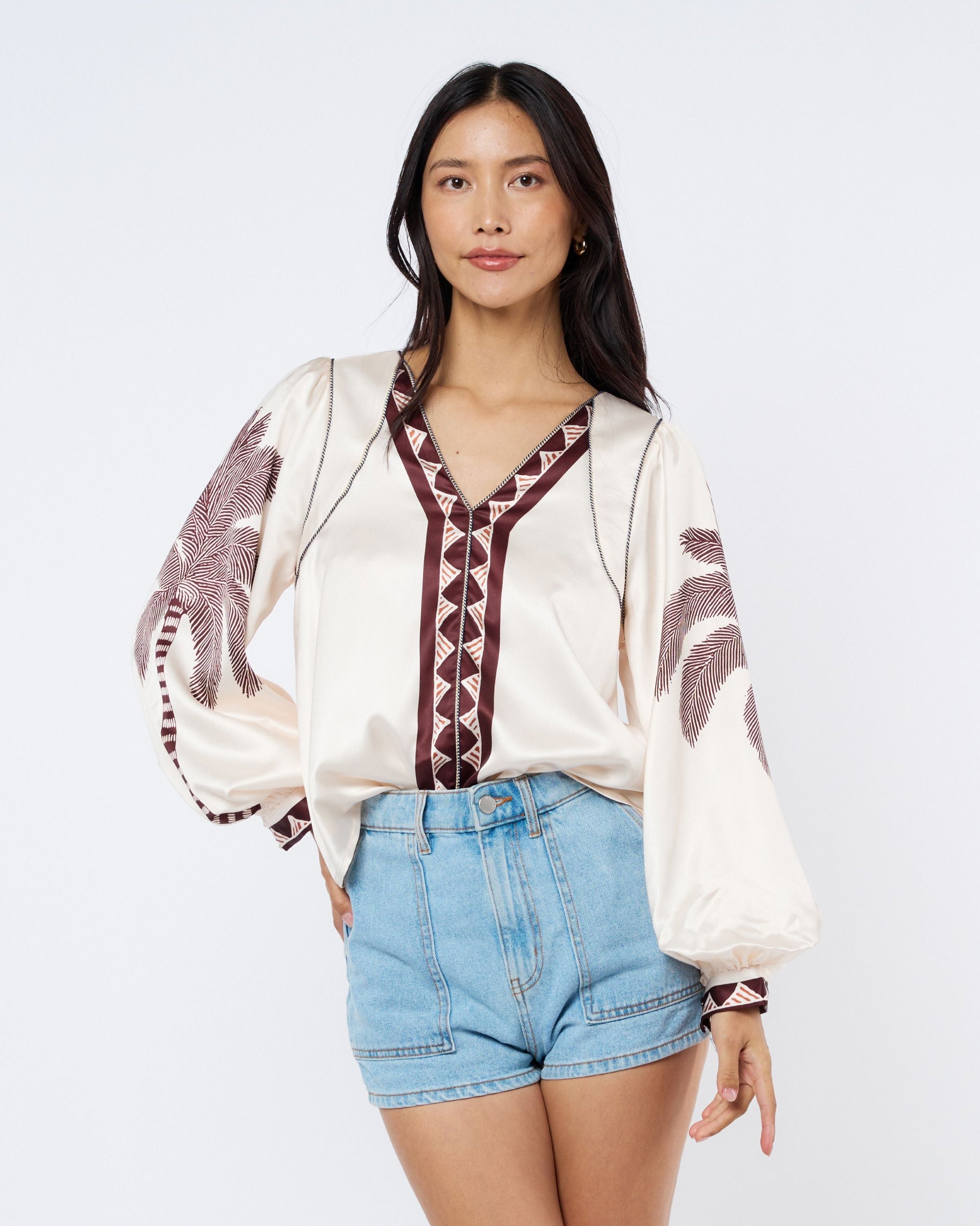Woman wearing a white blouse with embroidery and denim shorts on a white background