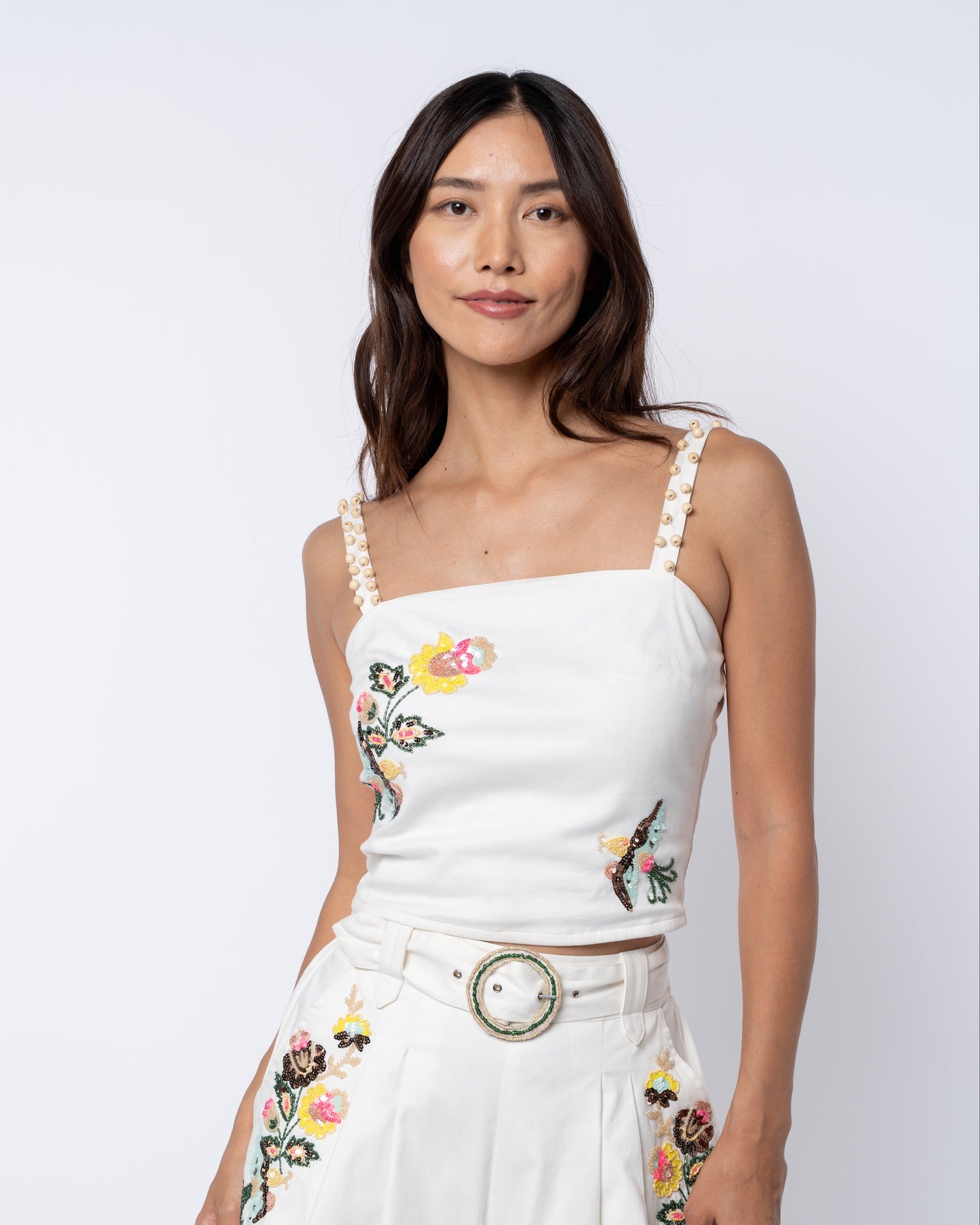 Woman wearing a white top and pants with floral embroidery on a plain background