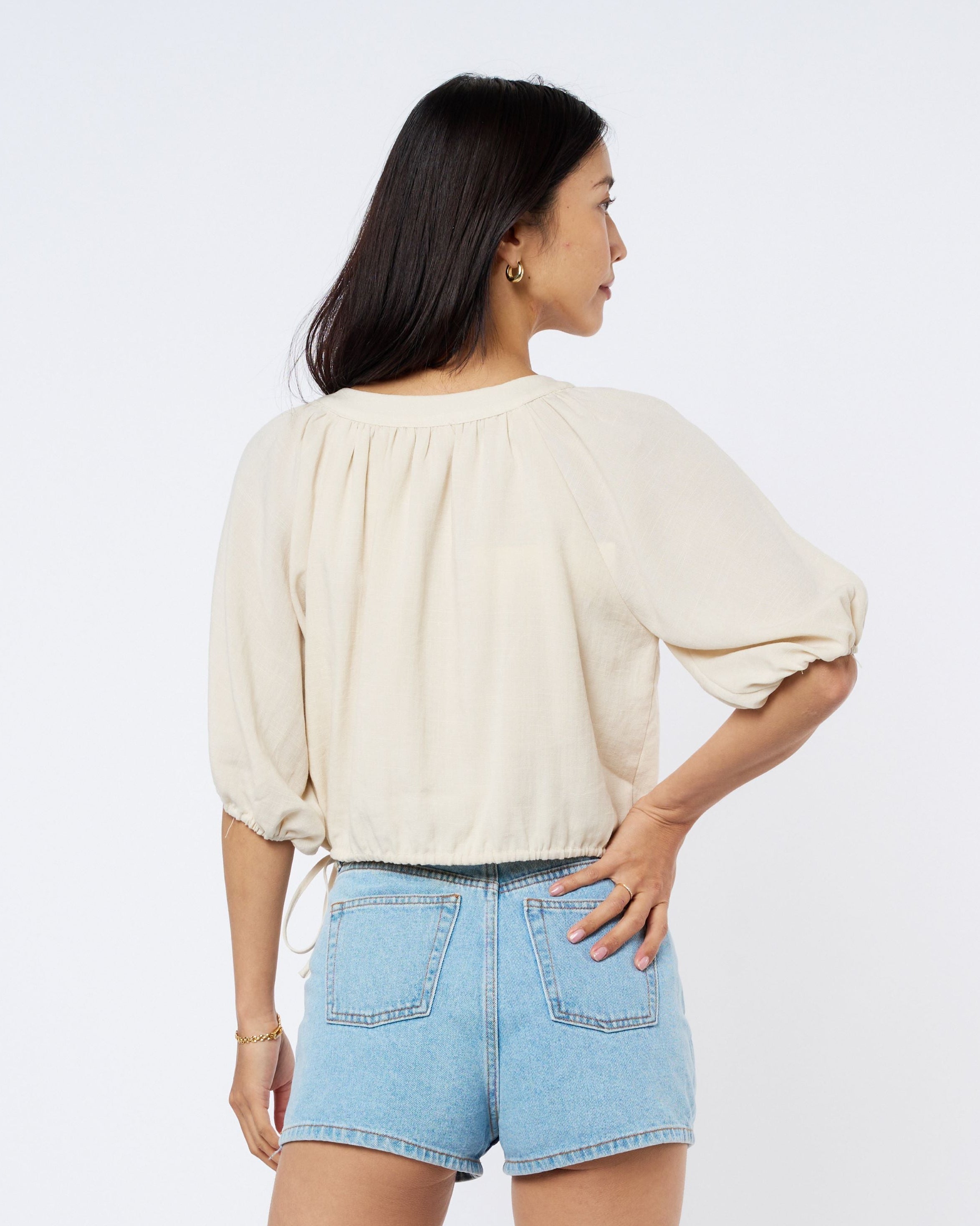 Woman wearing a cream blouse and light blue shorts on a white background