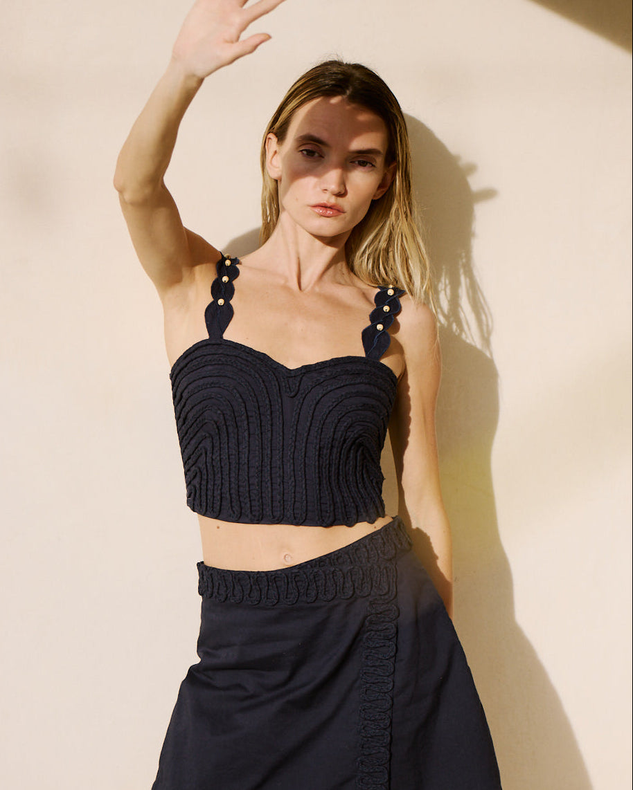 Woman wearing a black ribbed crop top and skirt against a beige wall.