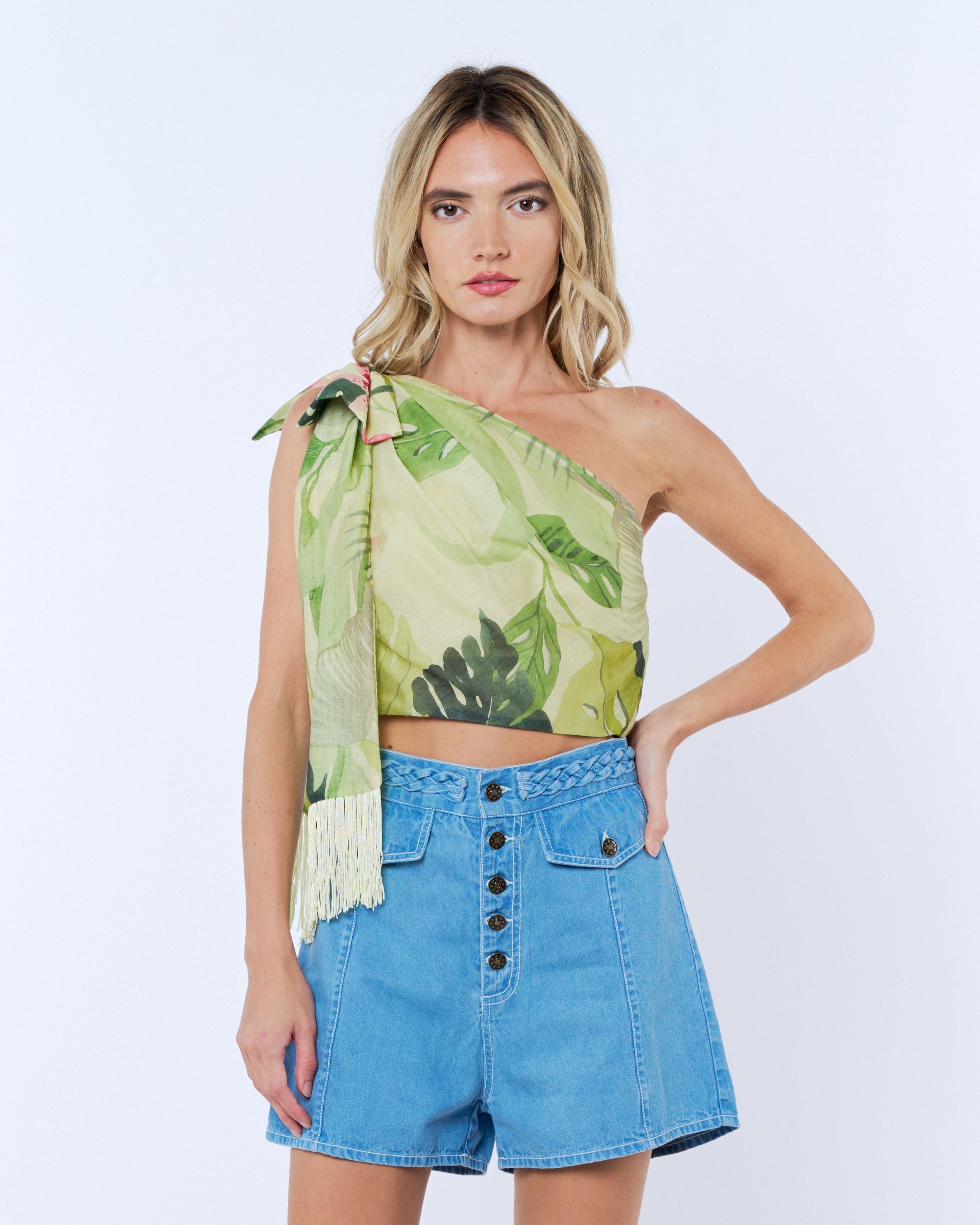 Woman wearing a green leaf-patterned top and blue denim shorts on a white background