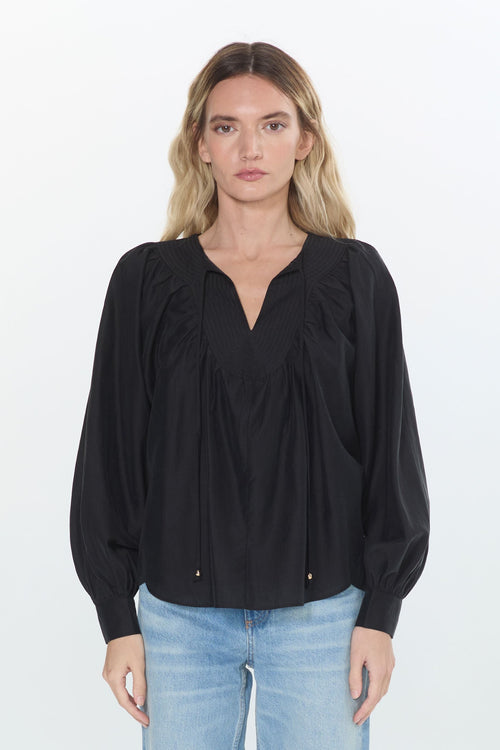 Cargar la imagen 1 en la vista de la galería. A woman stands against a plain white studio background wearing a black long-sleeve blouse with a gathered V-neck and light-wash blue jeans.