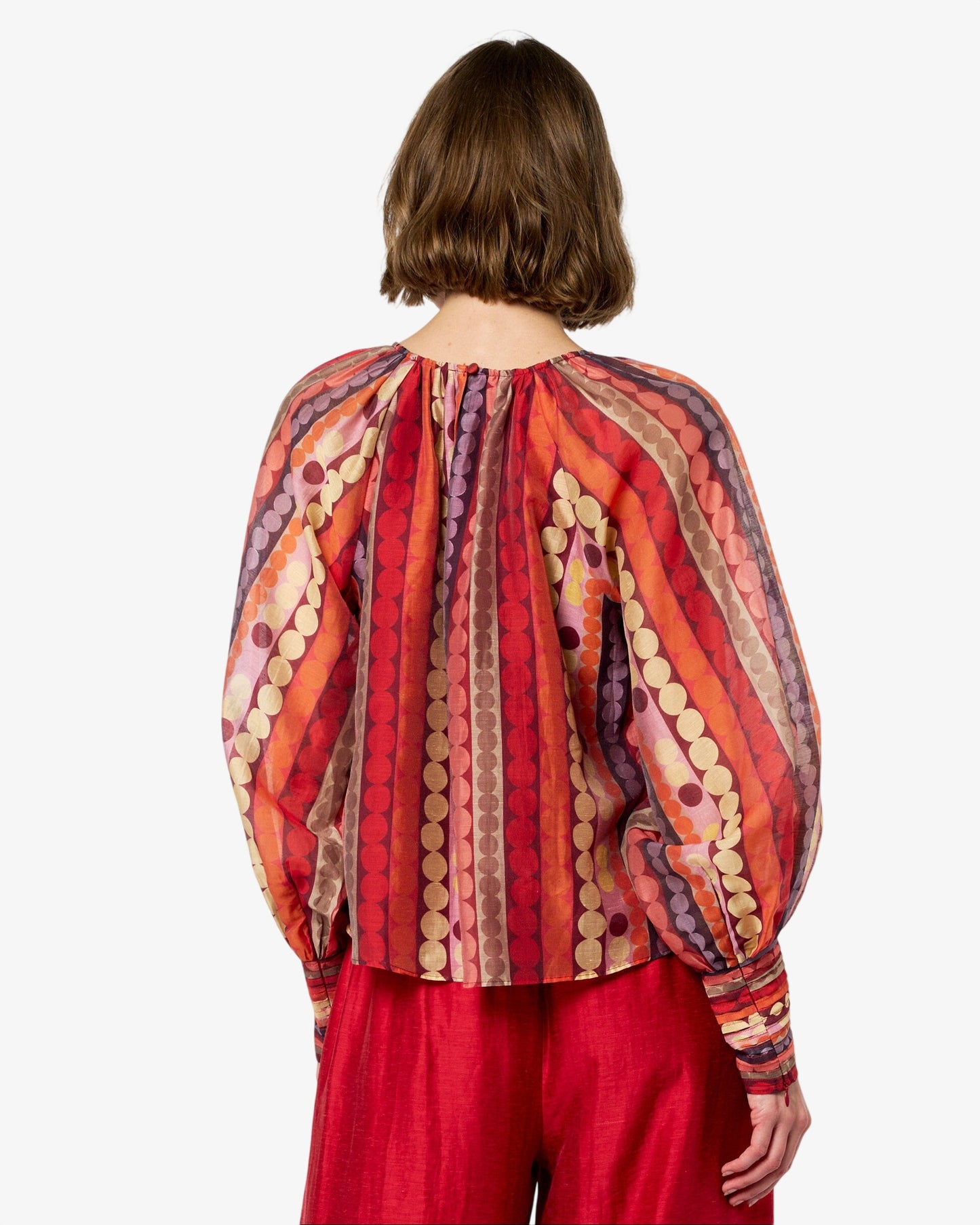 Person wearing a red patterned blouse and red pants on a white background