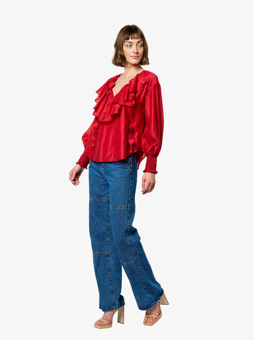 Load image 1 in gallery view. Woman wearing a red blouse with ruffles and blue jeans on a white background